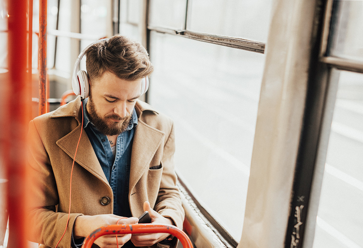 Junger Mann mit Bart sitzt im Bus und hört über seine Kopfhörer Musik